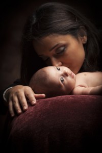 Young Attractive Ethnic Woman Holding Her Newborn Baby Under Dramatic Lighting.